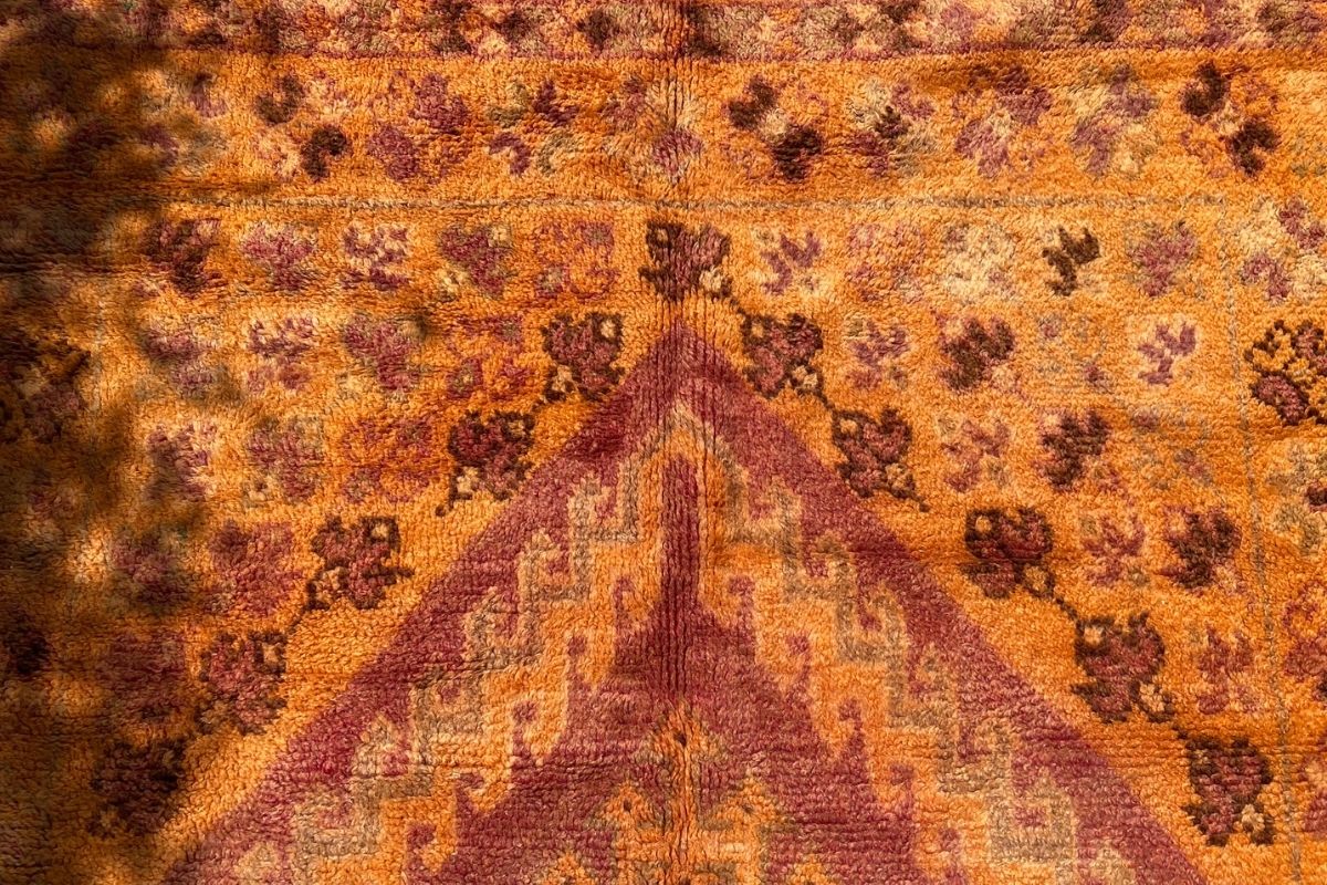 Detail of vintage Moroccan orange area rug with warm tones and pink Moroccan designs
