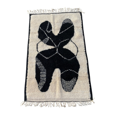 black graphic figure on a cream colored moroccan rug with black border collaboration rug between Kantara and Claudia Pearson
