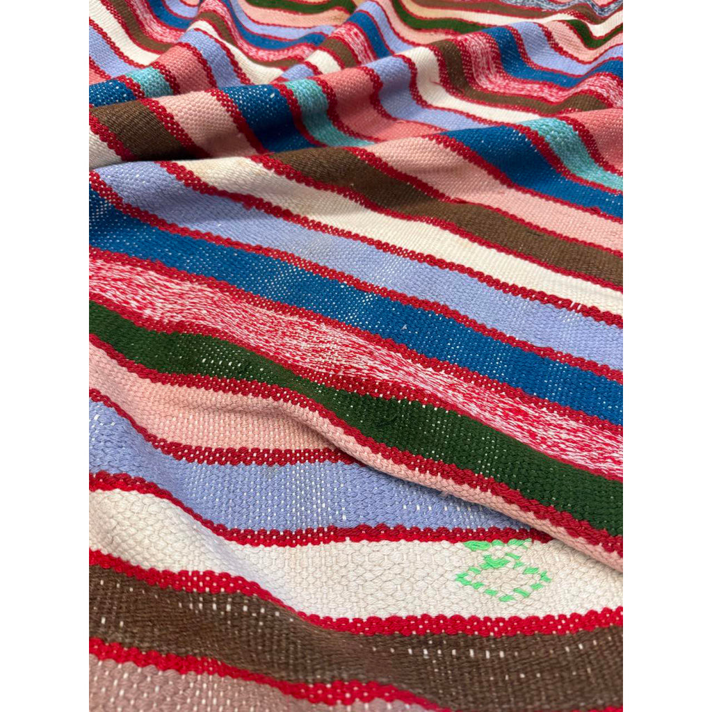 Close-up of multicolored striped vintage Moroccan blanket with a small green emblem.