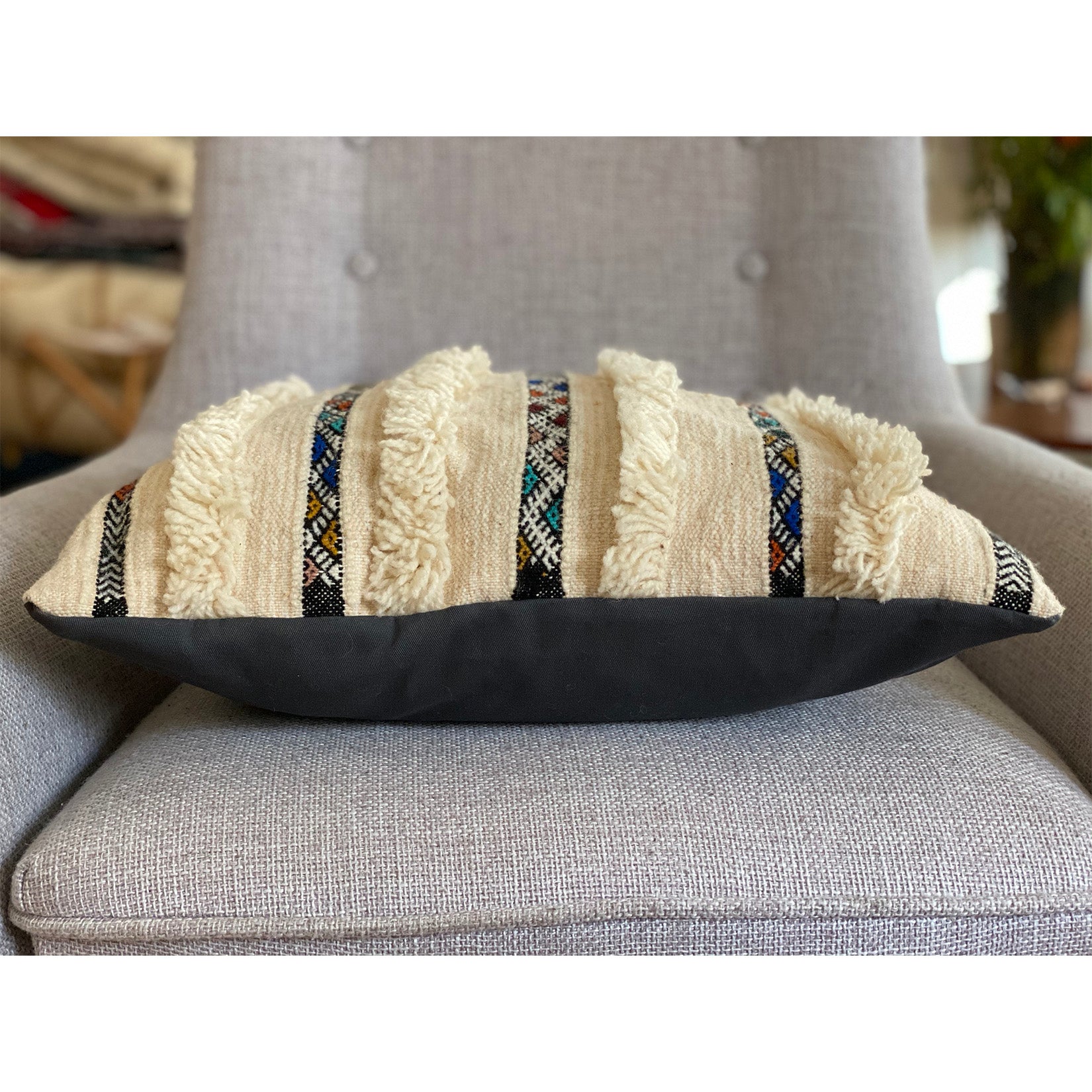 Side view of colorful Moroccan wedding blanket handira pillow on a grey mid century modern armchair