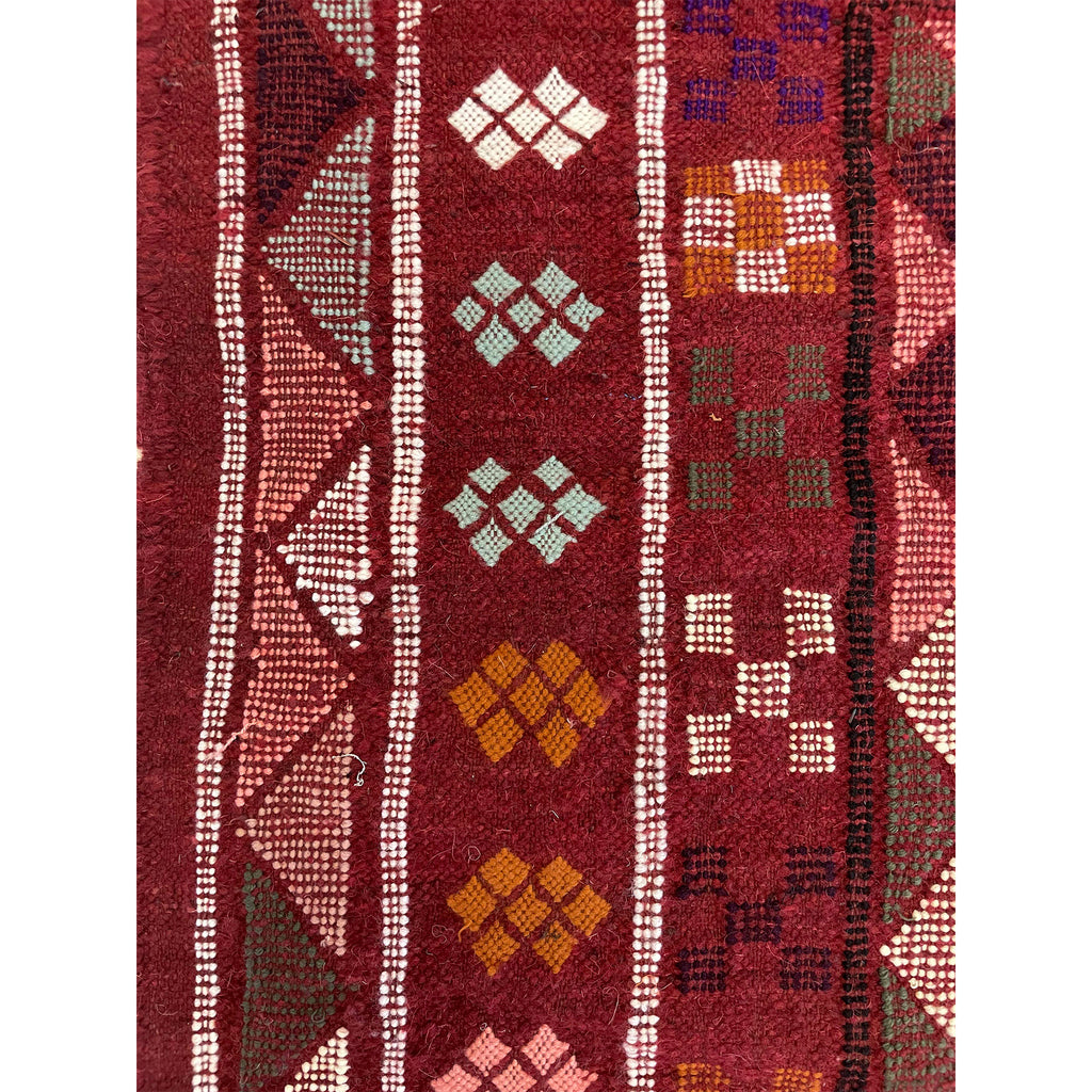 Close up of traditional border detail from Moroccan rug from the Middle Atlas Mountains on red background  | Kantara Moroccan Rugs in Los Angeles