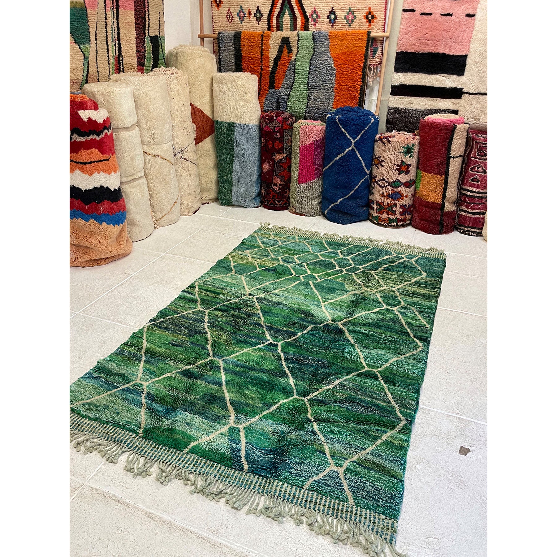 Green area sized Beni rug laid out on the floor in the Rug Shop with bundles of neutral oversized rugs in the background | Kantara Moroccan Rugs in Los Angeles at The Rug Shop